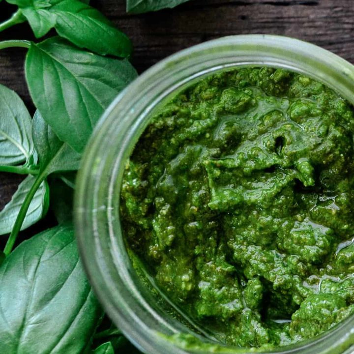 Basil pesto sauce in glass jar pictured with fresh basil leaves