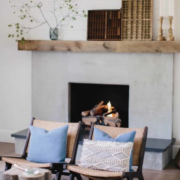 Cement fireplace with fire burning and reclaimed wood mantel with modern living room furniture