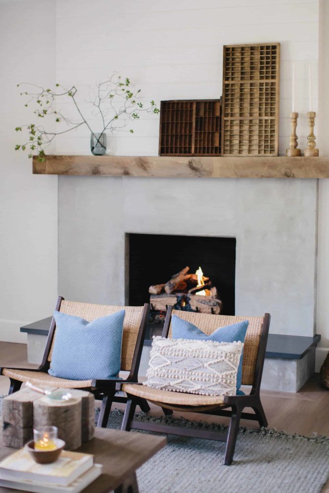 Cement fireplace with fire burning and reclaimed wood mantel with modern living room furniture