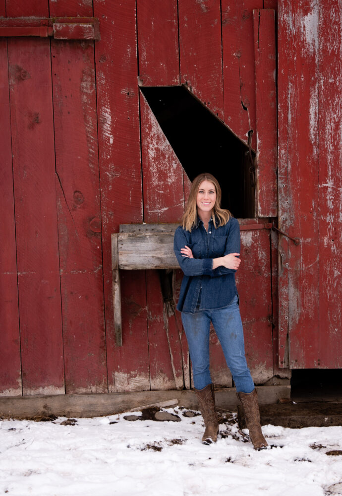 Girl standing in front of red barn in denim and boots