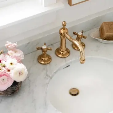 Brass faucet and marble counter in bathroom with pink flowers