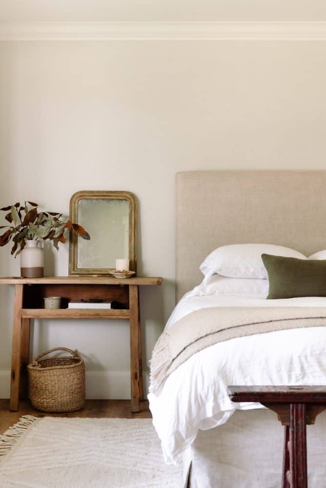 airy bedroom with grey walls and white rug with linen headboard and bench