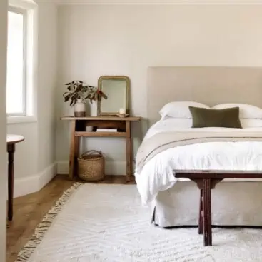 airy bedroom with grey walls and white rug with linen headboard and bench