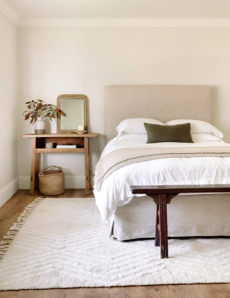 airy bedroom with grey walls and white rug with linen headboard and bench