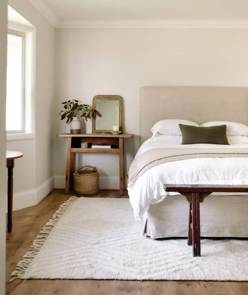 airy bedroom with grey walls and white rug with linen headboard and bench