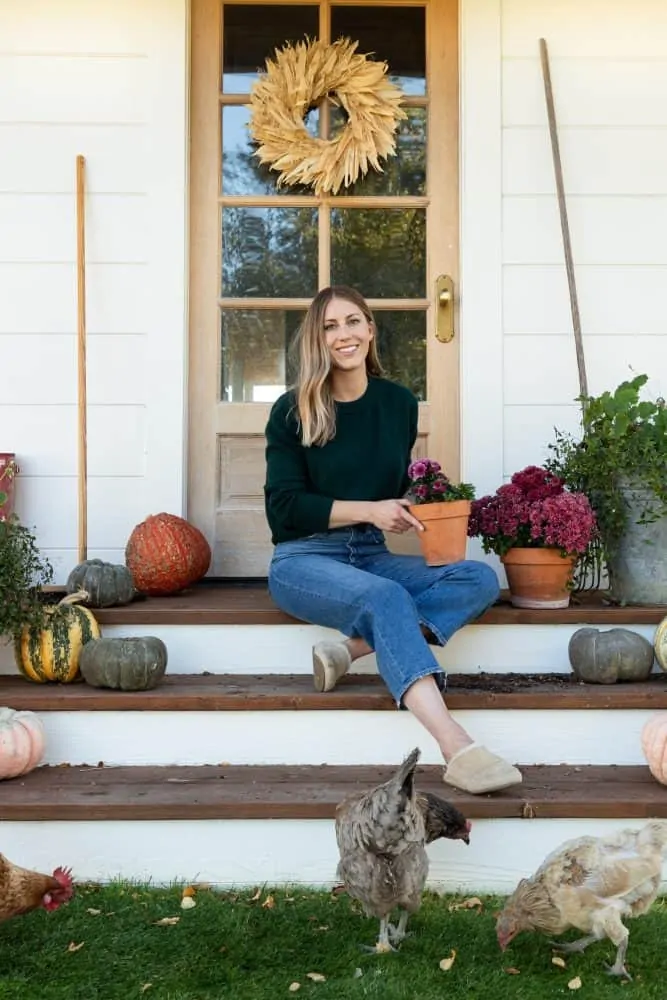 Girl sitting on porch with chickens on farmhouse porch with pumpkins
