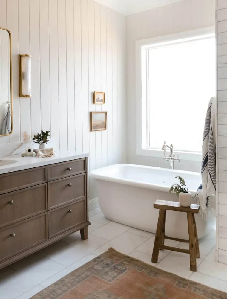 Grey bathroom with marble tile and oak vanity with free standing tub and vintage rug