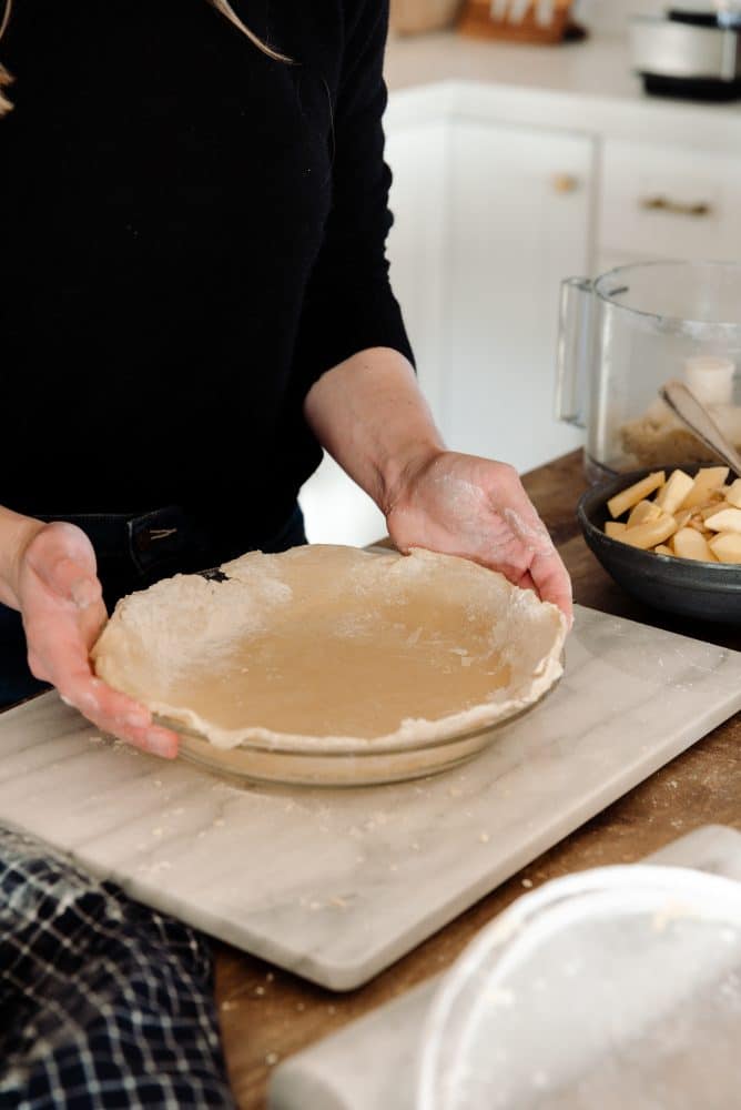 Person holding crust unbaked pie in farmhouse kitchen