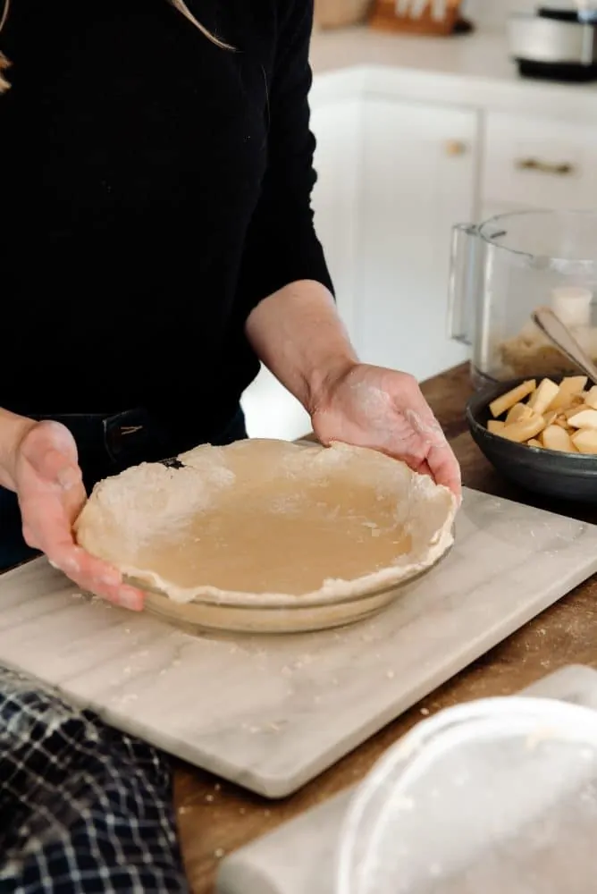 Person holding crust unbaked pie in farmhouse kitchen