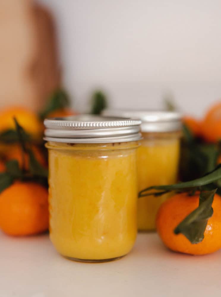 Jar of orange curd on countertop with mandarin oranges.