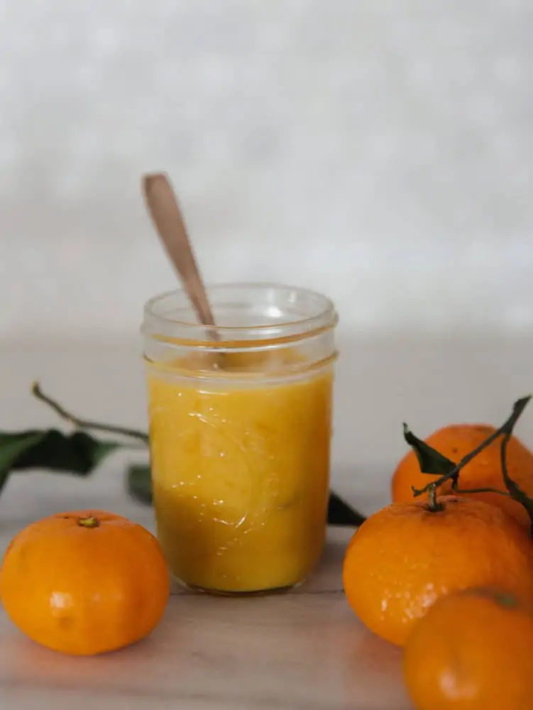 Jar of orange curd on countertop with mandarin oranges.
