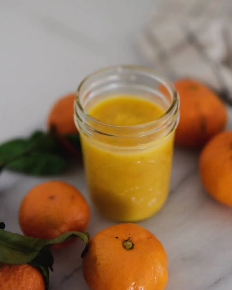 Jar of orange curd on countertop with mandarin oranges.