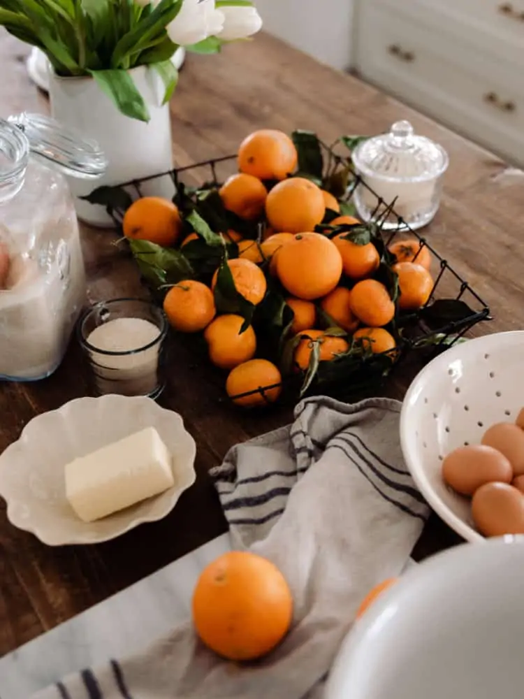 Ingredients for orange curd on wood countertop: oranges, butter, eggs, sugar.