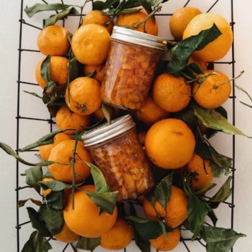Basket of oranges with jars of orange marmalade sitting on top.