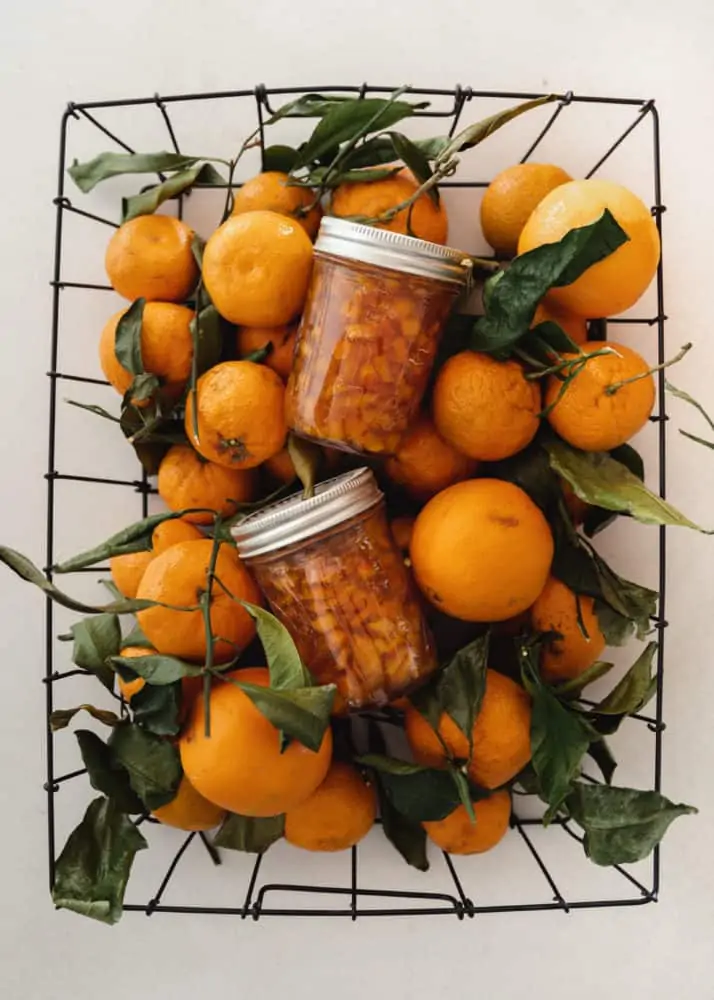 Basket of oranges with jars of orange marmalade sitting on top.