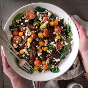 A beautiful steak salad topped with tomatoes in a large white salad bowl.