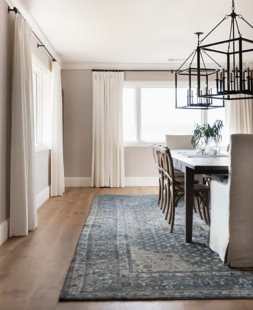 Modern farmhouse dining room with light streaming in the windows. Blue patterned rug under a long farmhouse table.