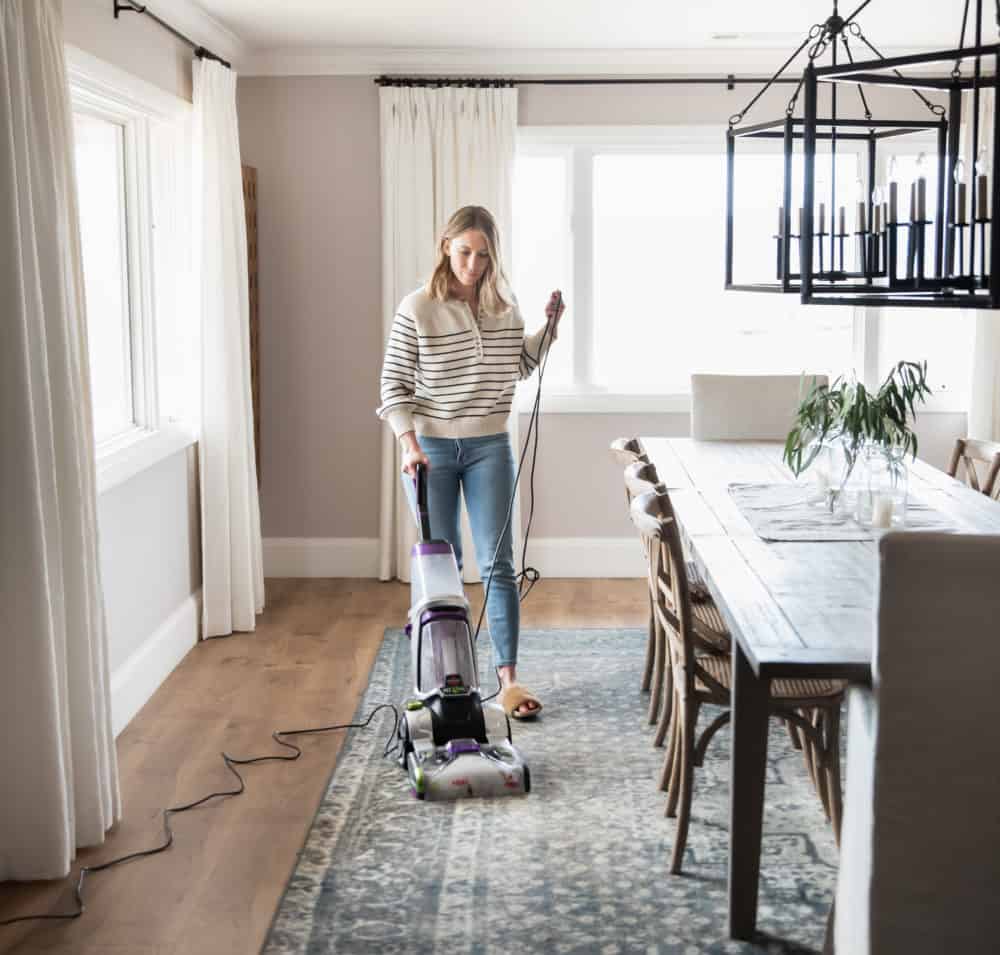 Woman vacuuming dining room carpet with Bissell carpet cleaner.