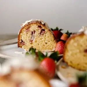 Side view of a slice of strawberry cake on white plate with fresh strawberries.