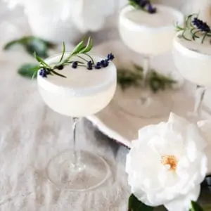 Lavender vodka fizz cocktail on a table with roses and rosemary on a table.