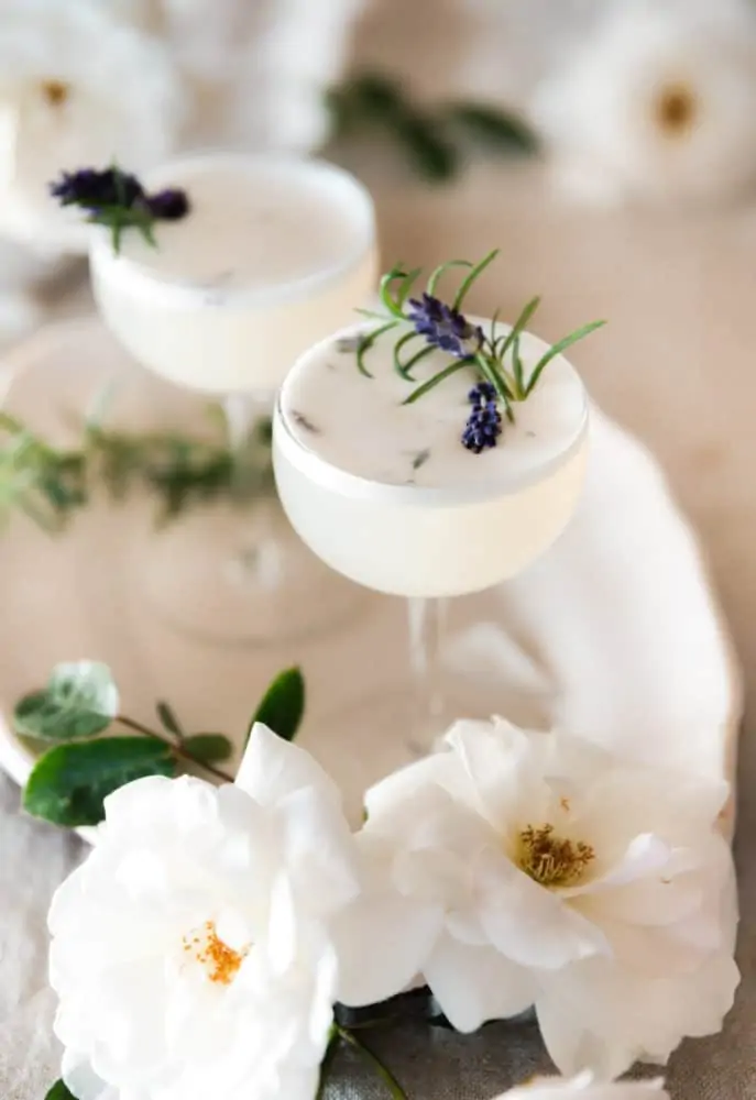 Lavender vodka fizz cocktail on a table with roses and rosemary on a table.