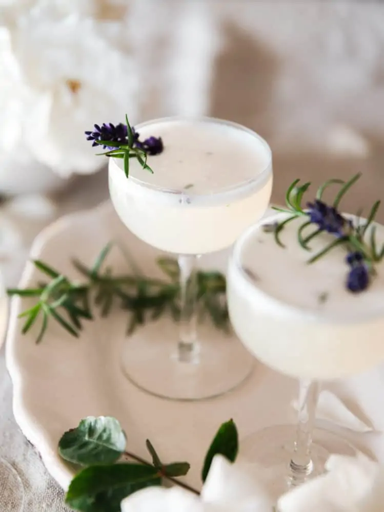 Lavender vodka fizz cocktail on a table with roses and rosemary on a table.