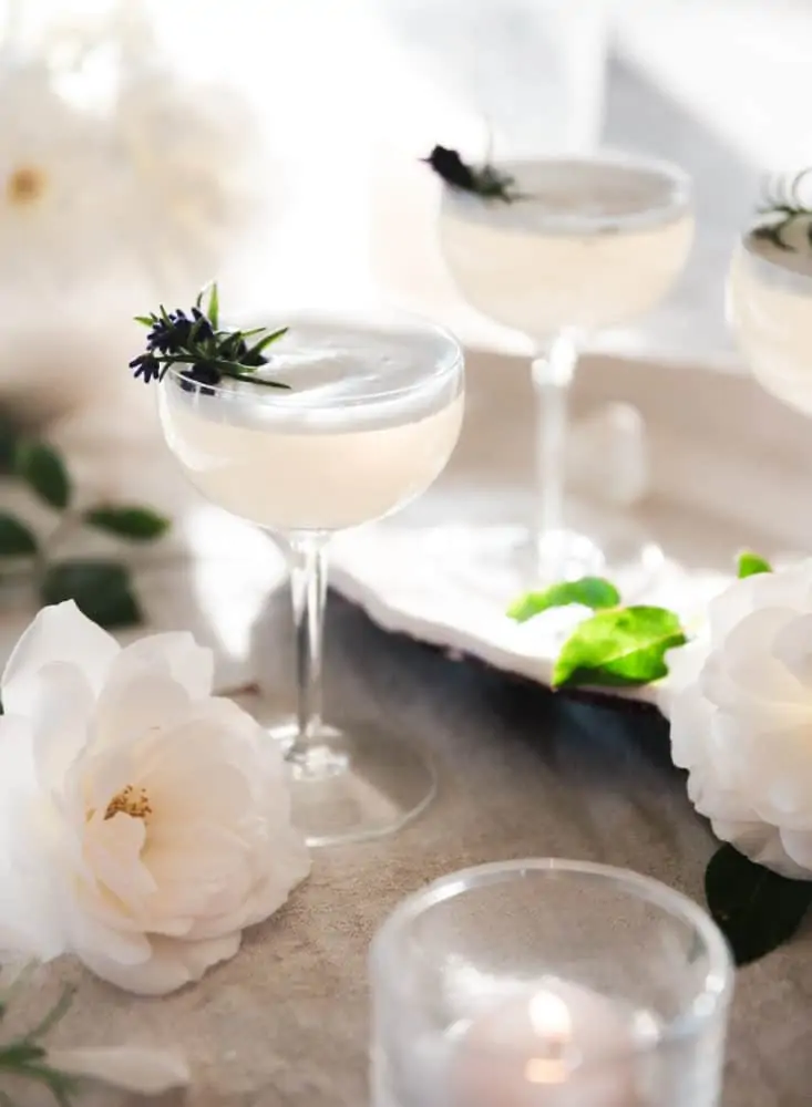 Lavender vodka fizz cocktail on a table with roses and rosemary on a table. 