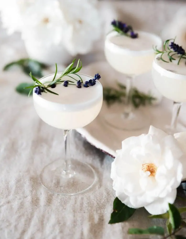 Lavender vodka fizz cocktail on a table with roses and rosemary on a table.