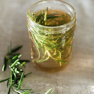 Mason jar of rosemary simple syrup on linen backdrop.