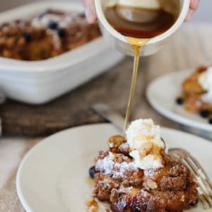 An up close image of baked french toast served on a white plate with maple syrup poured over the top.