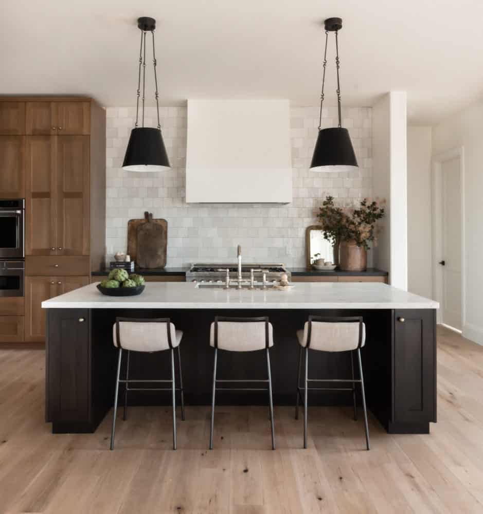 Beautiful kitchen design with black island and oak cabinetry with marble countertops.