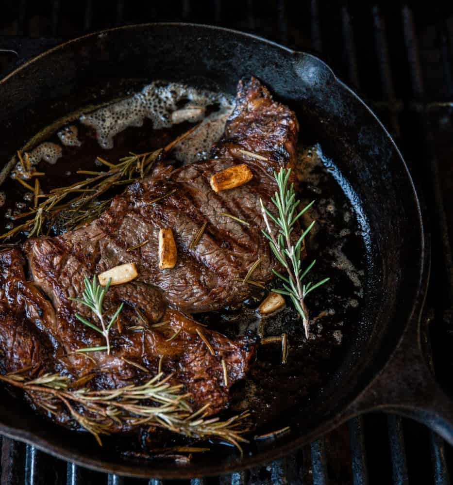 Ribeye steak on cast iron skillet with seasoning and rosemary.