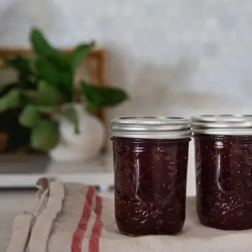 Two sealed masons jars filled with fig jam resting on a striped kitchen towel.