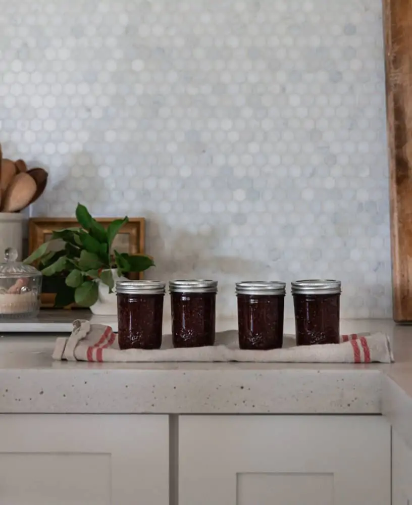A row of four canned mason jars of fig jam on a kitchen towel.