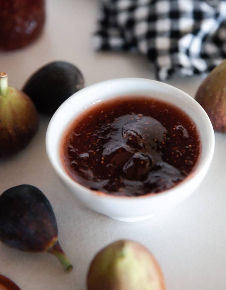 A white bowl of fig jam surrounded by figs.