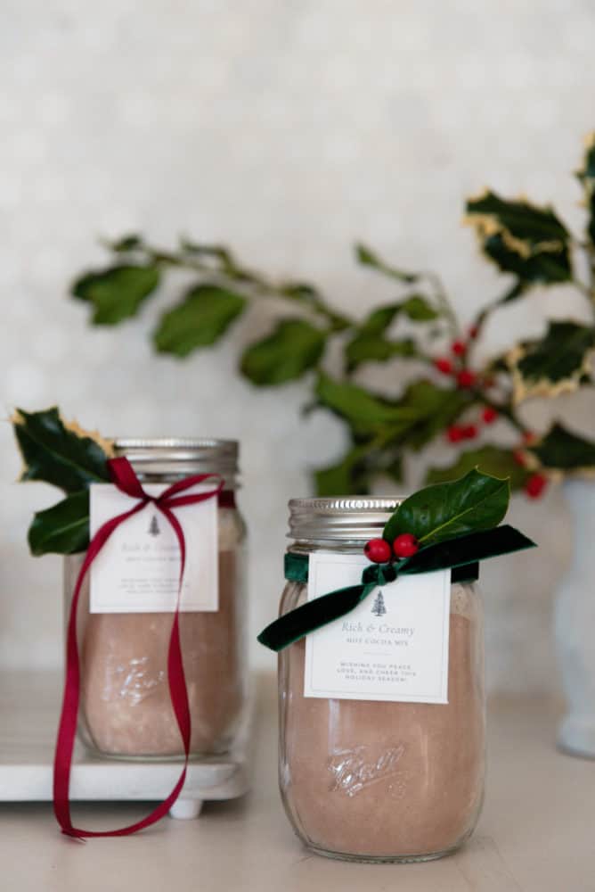 Jar of homemade hot chocolate mix with free printable gift tag and green velvet ribbon on concrete countertop in farmhouse kitchen.