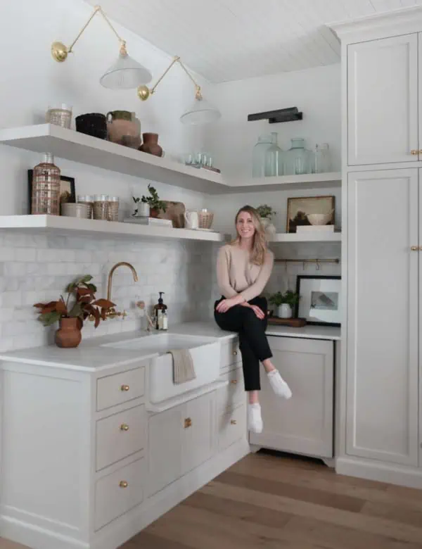 Small modern farmhouse kitchen with brass hardware, open shelving, and marble backsplash with the interior designer sitting on top of the counter.