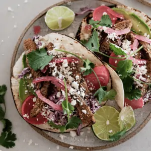 Two steak tacos on a plate with lime wedges