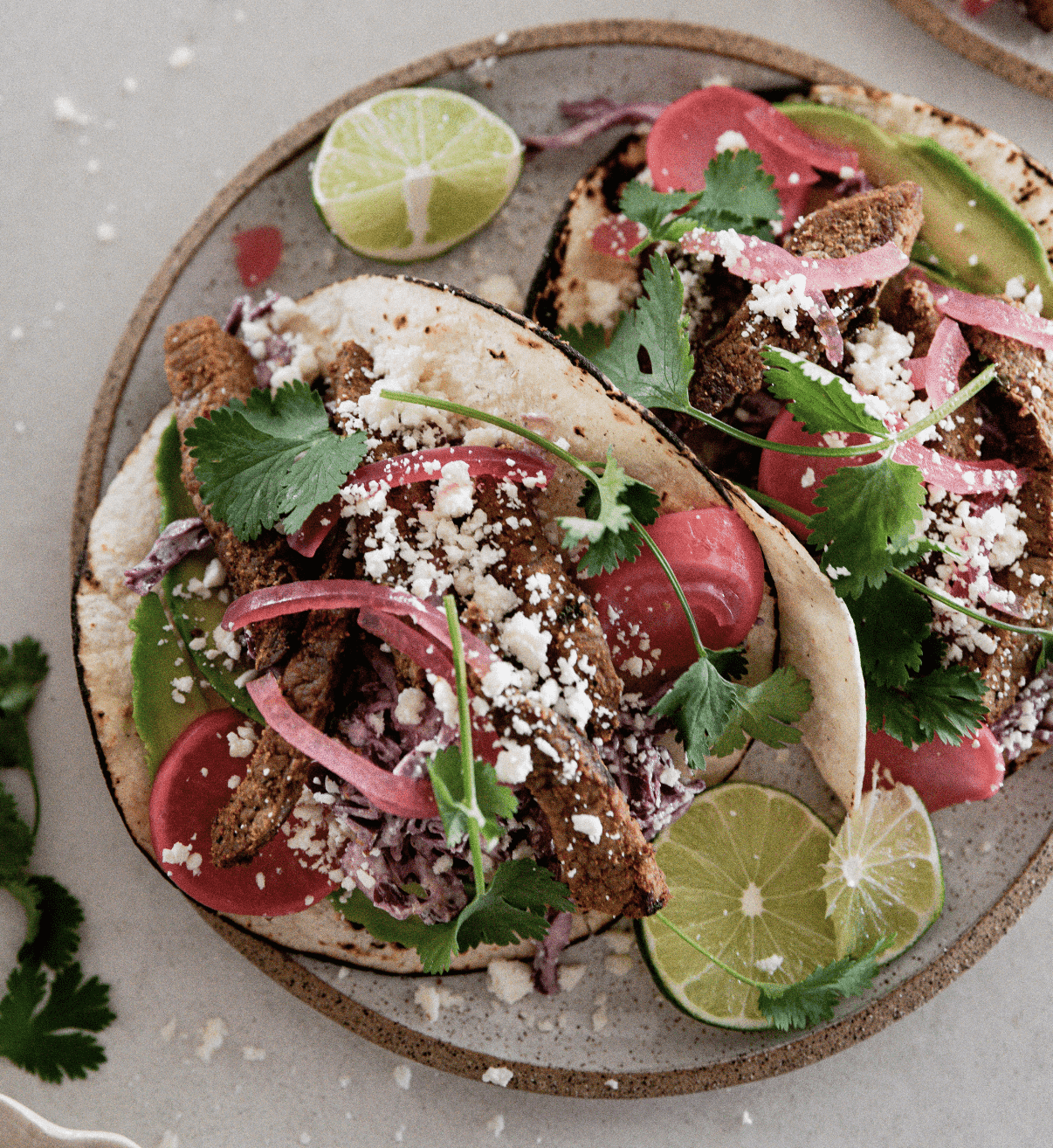 Two steak tacos on a plate with lime wedges