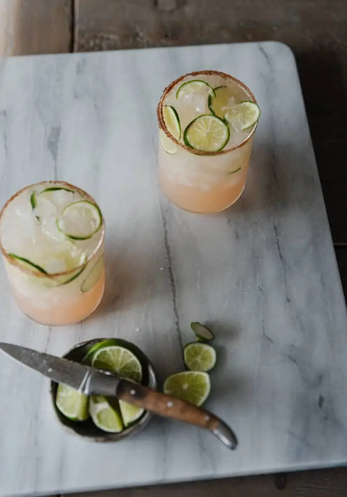 2 Paloma drinks on a marble cutting board with cut lime wedges in a bowl