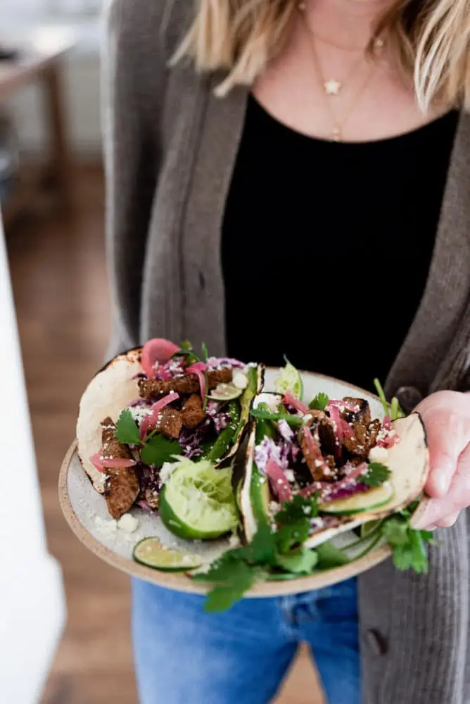 A woman holding a plate of steak tacos