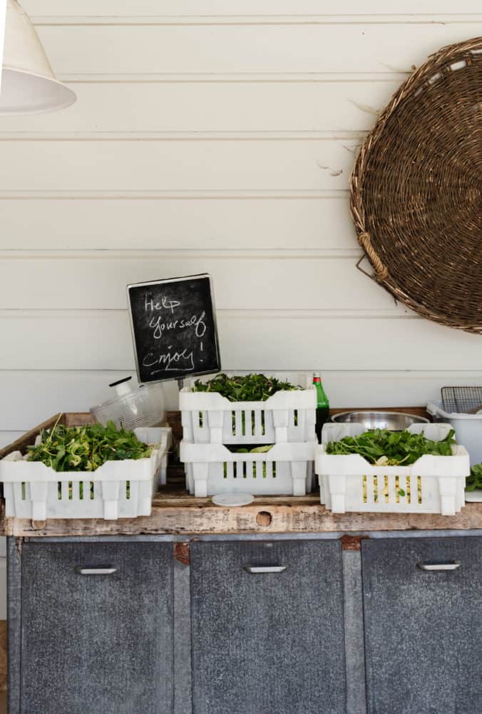 rustic sideboard with white crates filled with fresh greens options and a small chalkboard saying "help yourself enjoy"