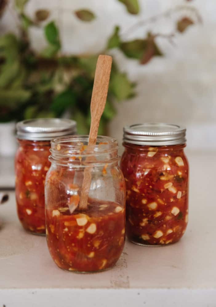 three jars of salsa, the forefront jar is open with a wooden spoon inside