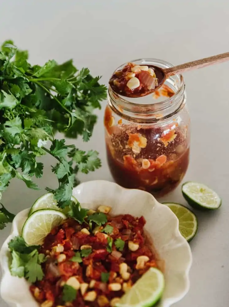 bowl of salsa with limes and cilantro and the jar of salsa in the background