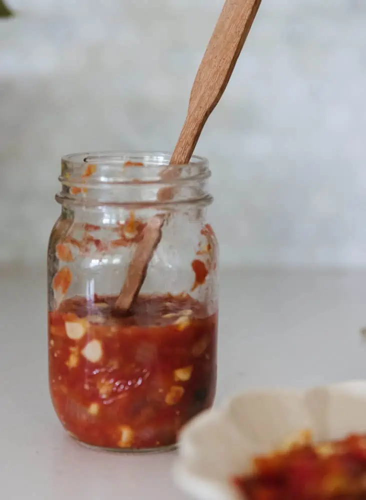 open glass jar of salsa with wooden spoon inside