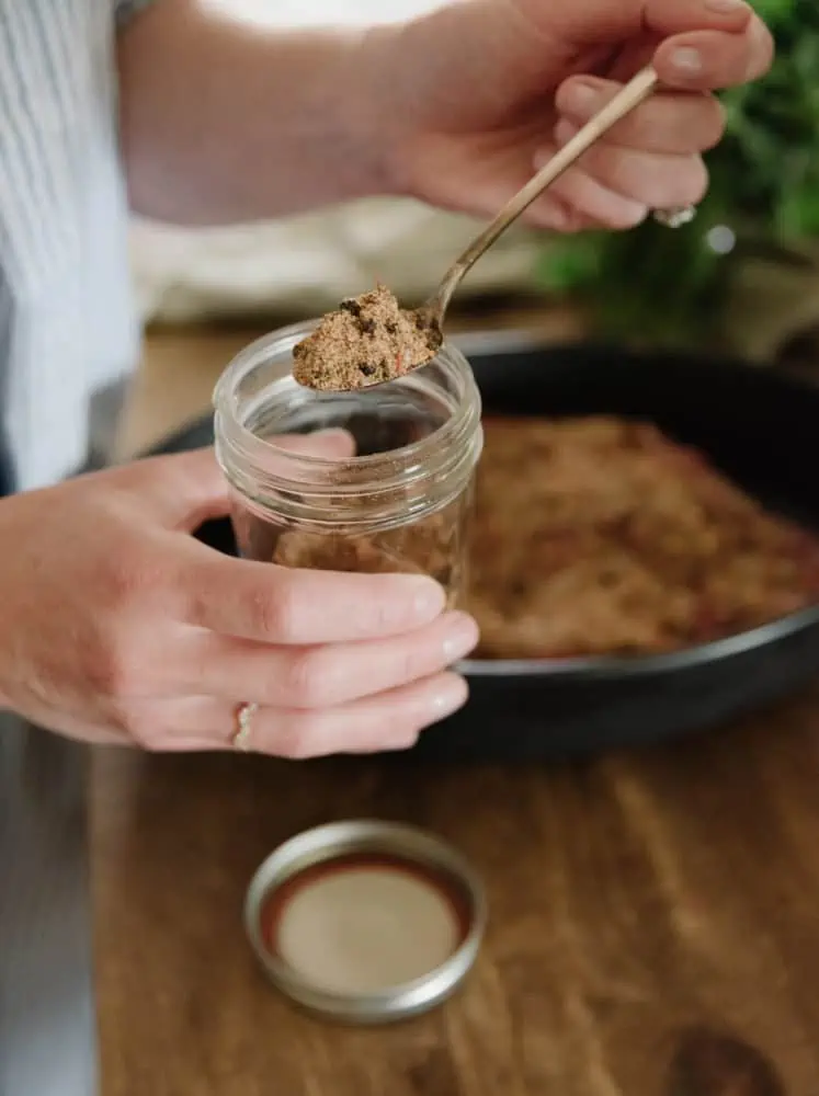 close up photo of a woman's hands holding a jar of homemade seasoning with a spoon full scooped out