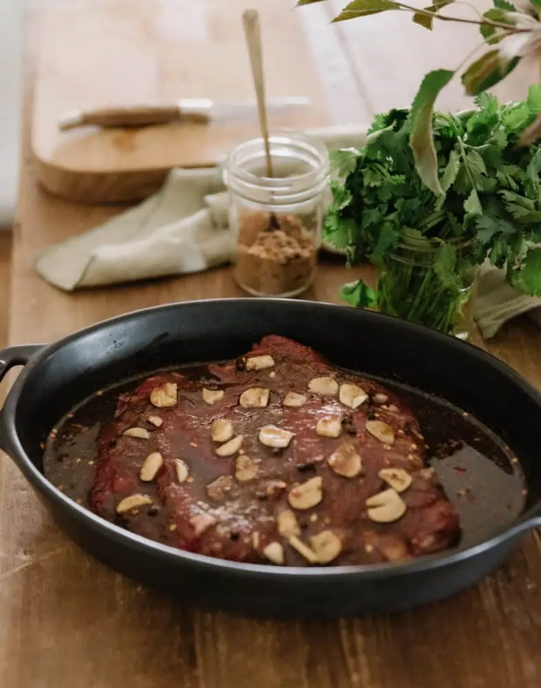 flank steak in a cast iron skillet on a butcher block countertop with spices in the background