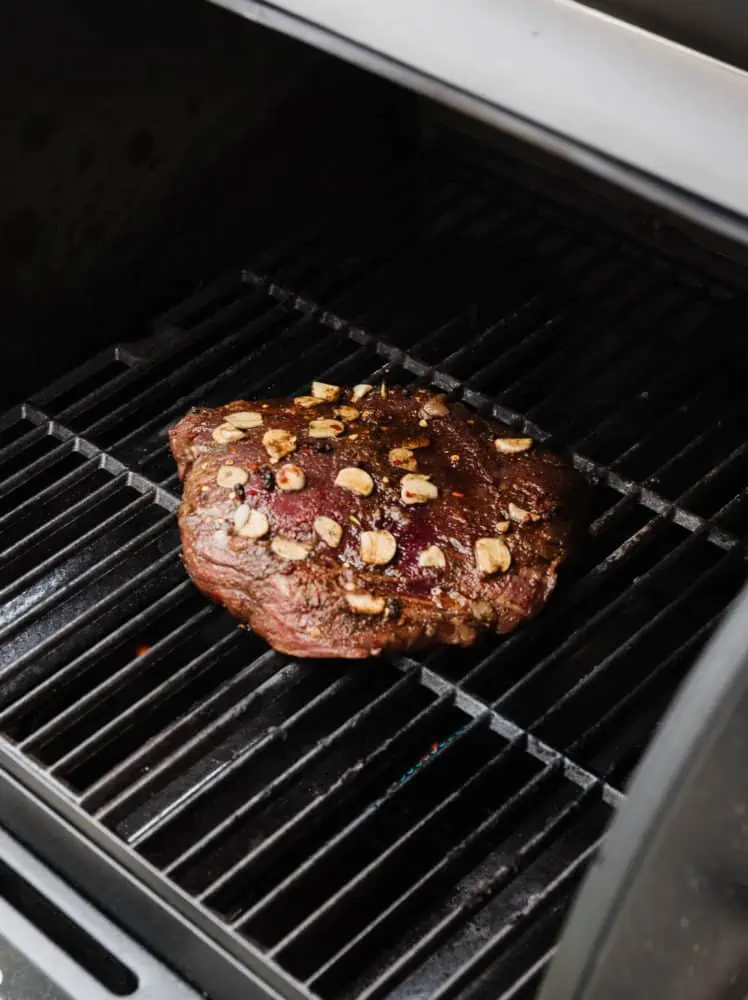 flank steak on a grill with sliced garlic on top