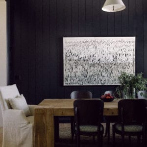 black walls with a rustic wood dining table surrounded by vintage chairs and a large black and white painting on the wall