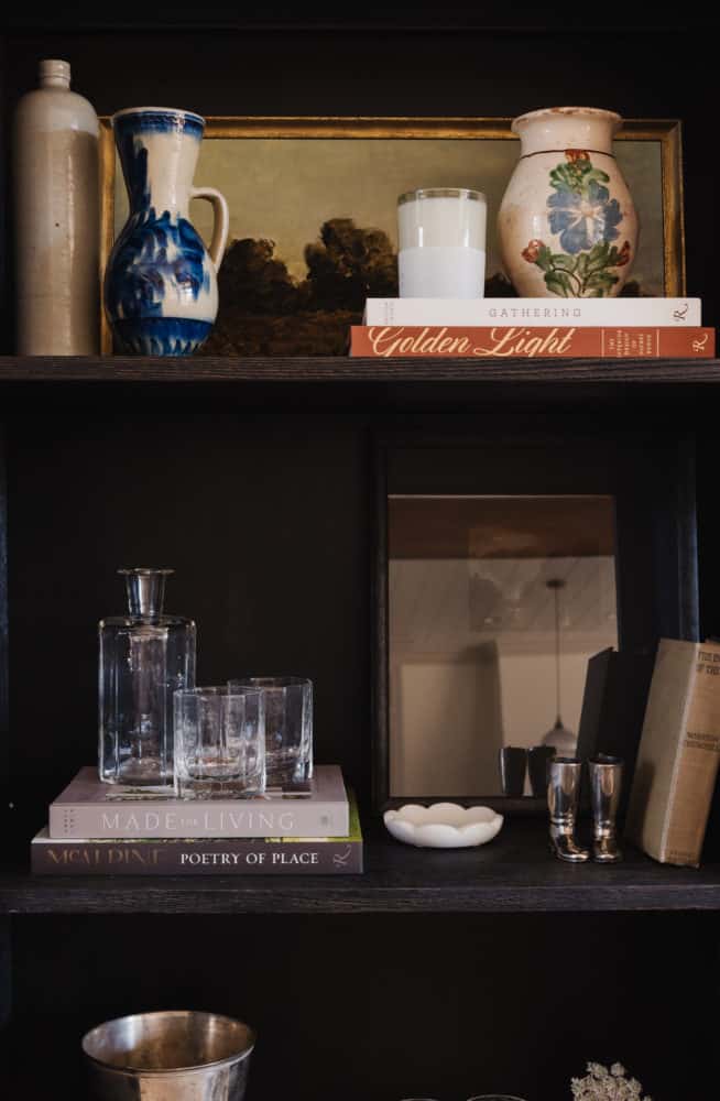 close up photo of shelving styling with layers of artwork, books, and decorative objects.